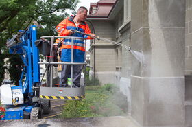 Worker applies the graffiti protection to the building in a pallet truck